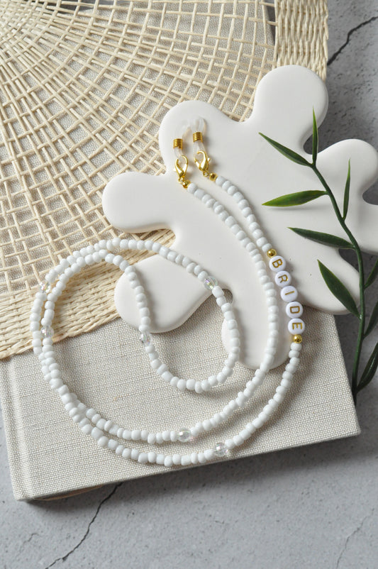 Beaded glasses chain with "Bride" inscription displayed on a grey and off-white background, with a splash-shaped stone positioned above the chain.