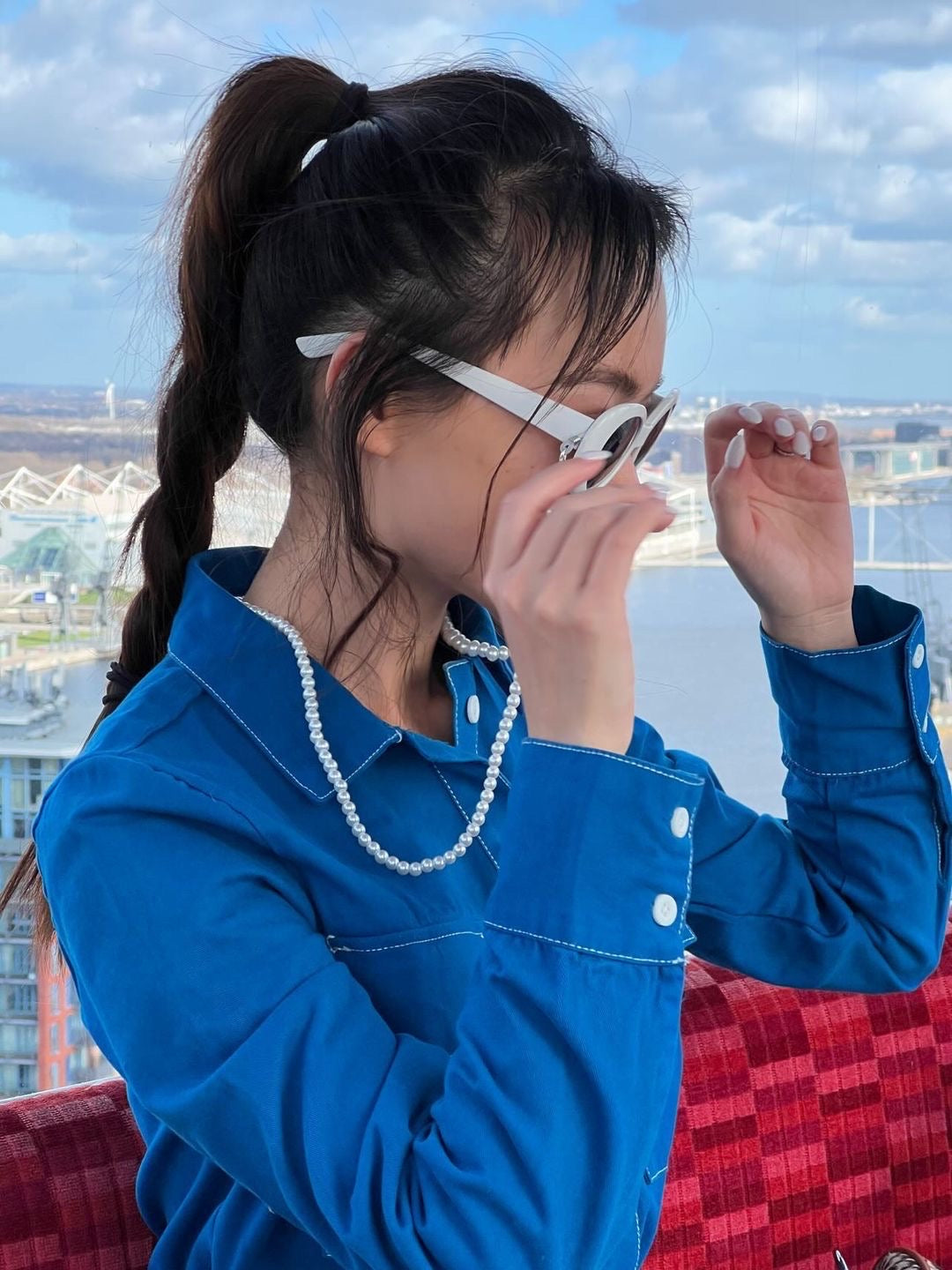 A girl in a blue shirt models our glasses necklace against a backdrop of blue skies. The necklace adds a stylish touch to her outfit, complementing the clear, sunny background.