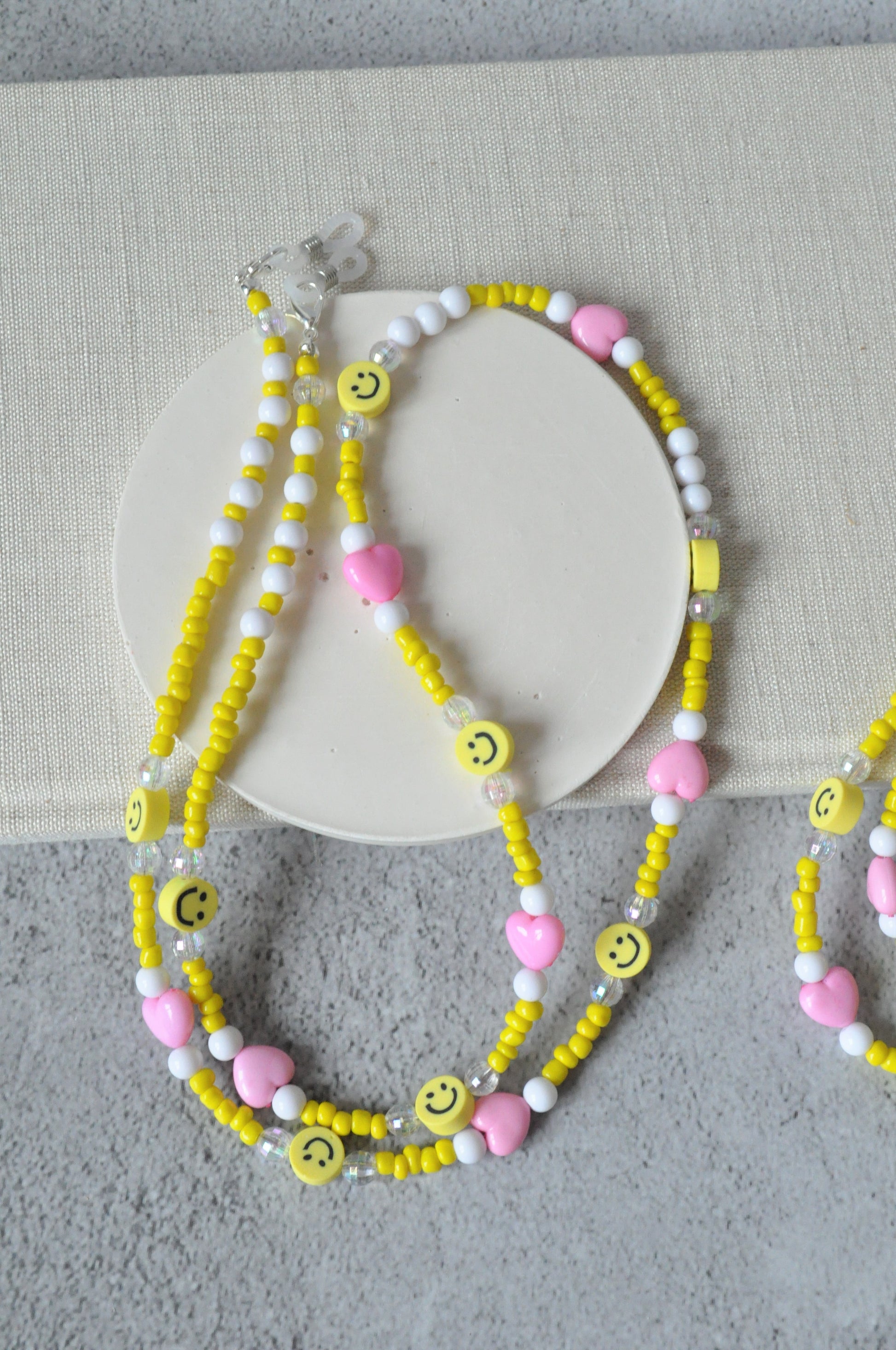 On a grey background, a textured notebook is positioned with the smiley beaded glasses chain