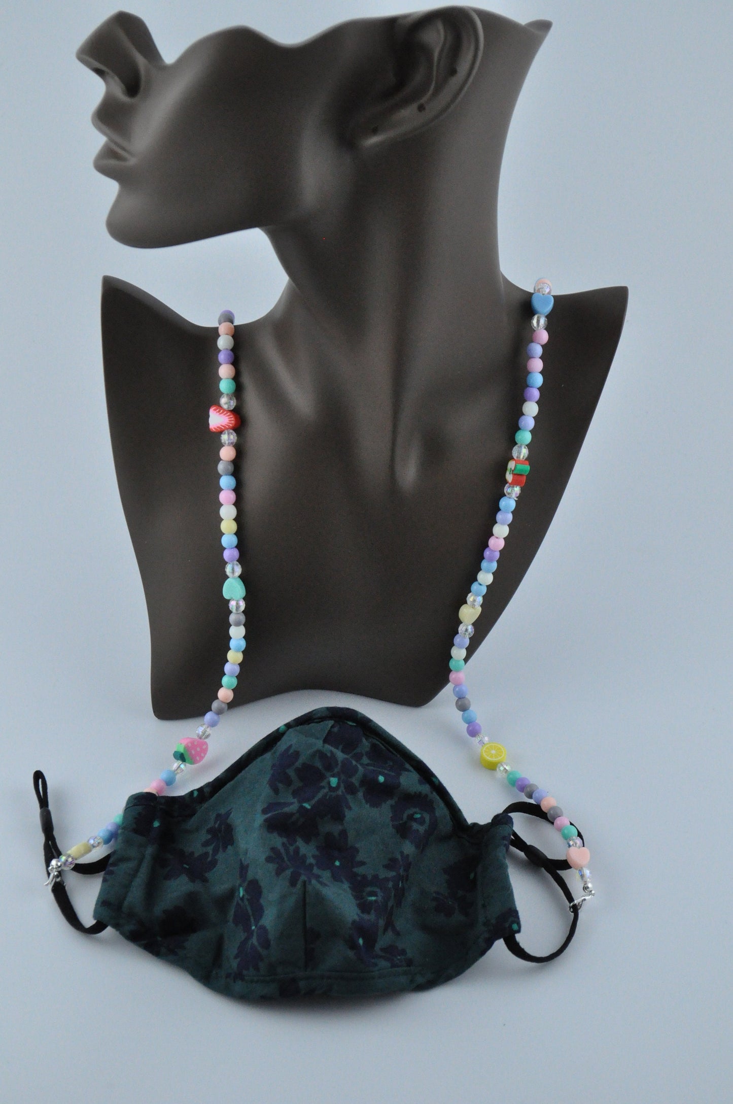 Close-up of the Fruit Salad Pastel Beaded Glasses Chain styled as a mask necklace on a jewellery mannequin head, with the focus on the chain against a grey background.