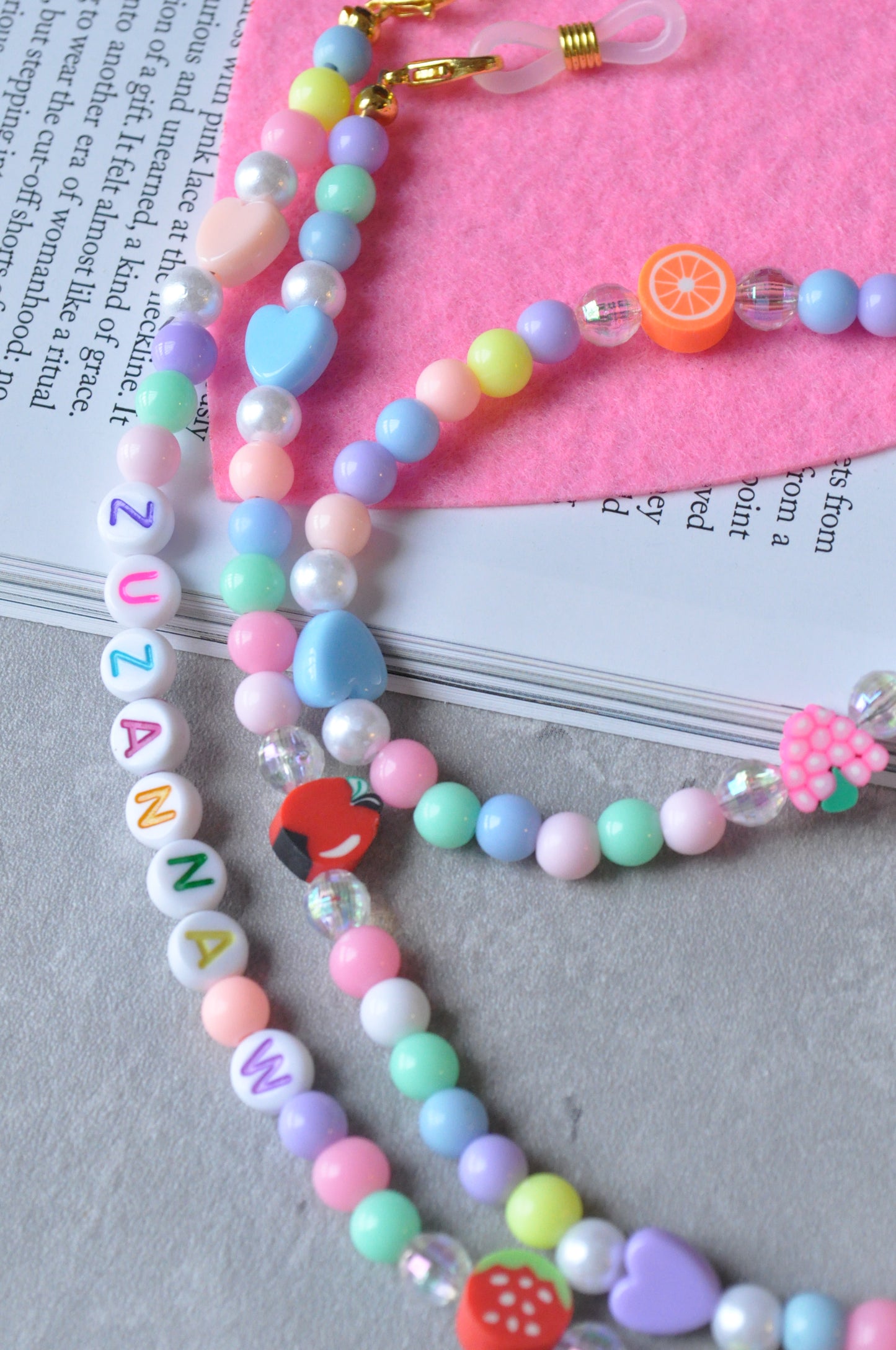 Close-up of the Fruit Salad Pastel Beaded Glasses Chain, highlighting the personalised letters against a grey background.