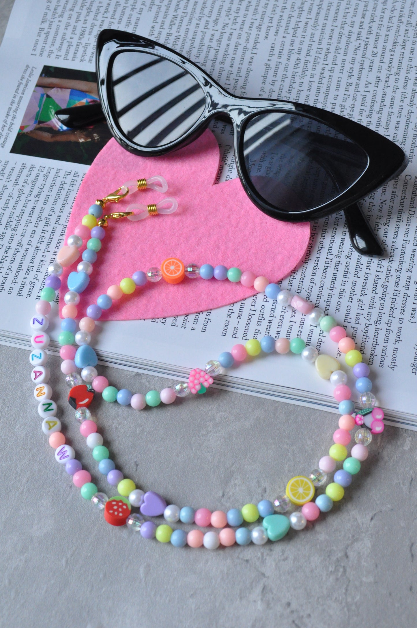 Fruit Salad Pastel Beaded Glasses Chain displayed on pink heart-shaped felt fabric, set against a grey background.