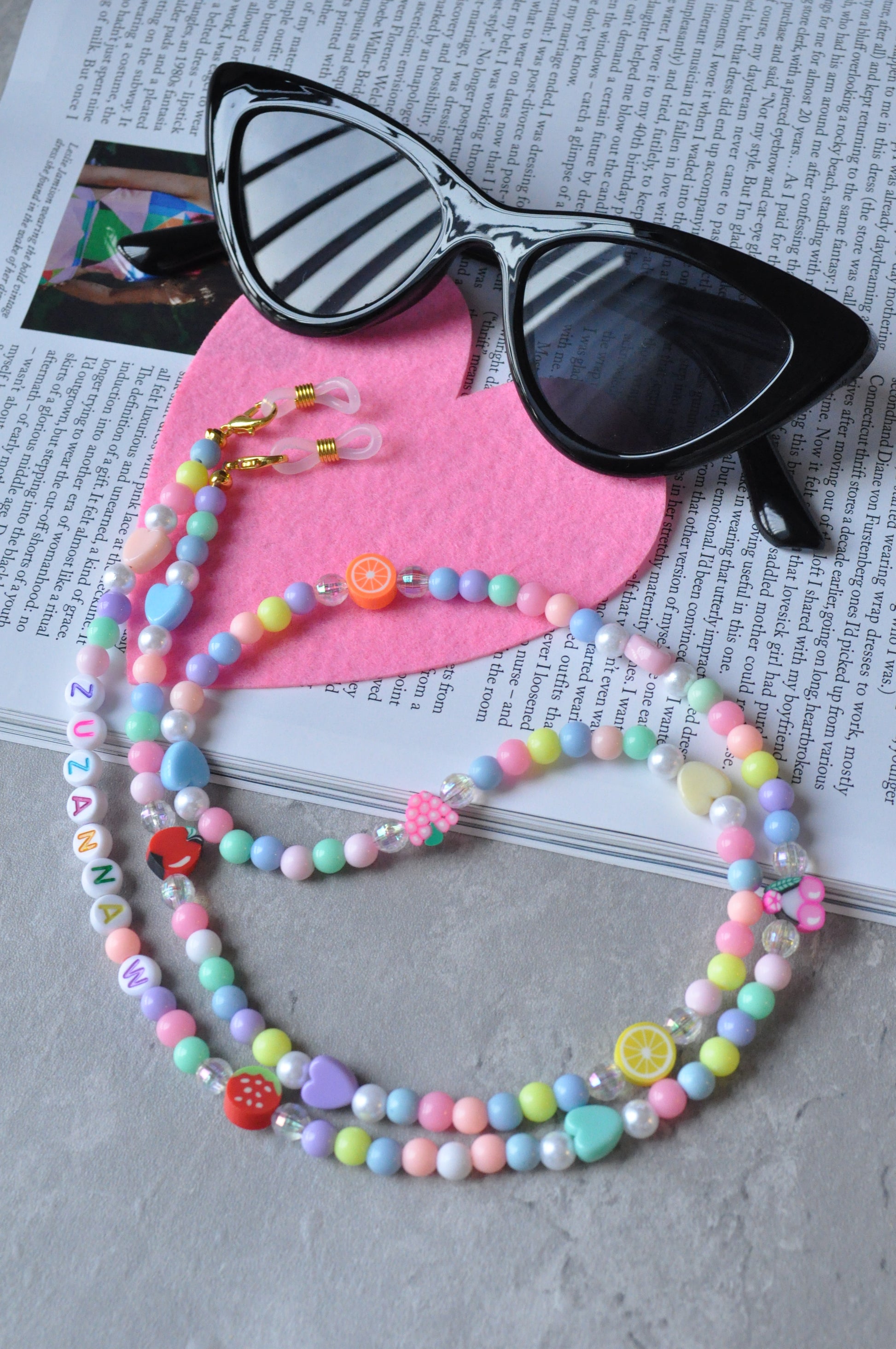 Fruit Salad Pastel Beaded Glasses Chain displayed on pink heart-shaped felt fabric, set against a grey background.
