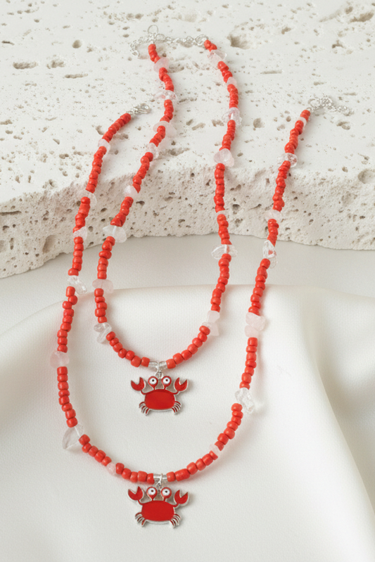 Red beaded necklace with crab pendants on a textured surface