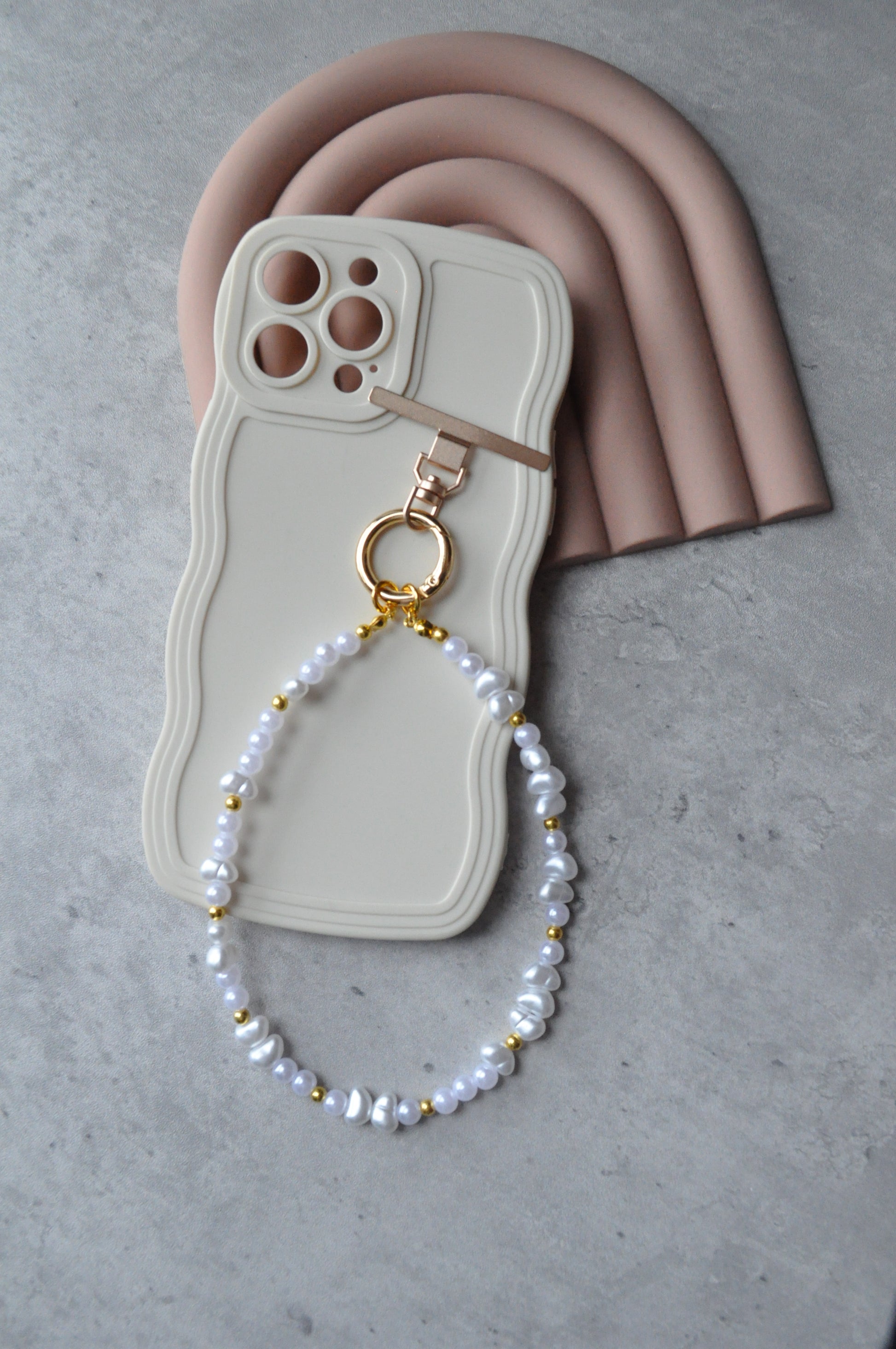 Phone case with a pearl necklace draped over it on a gray surface