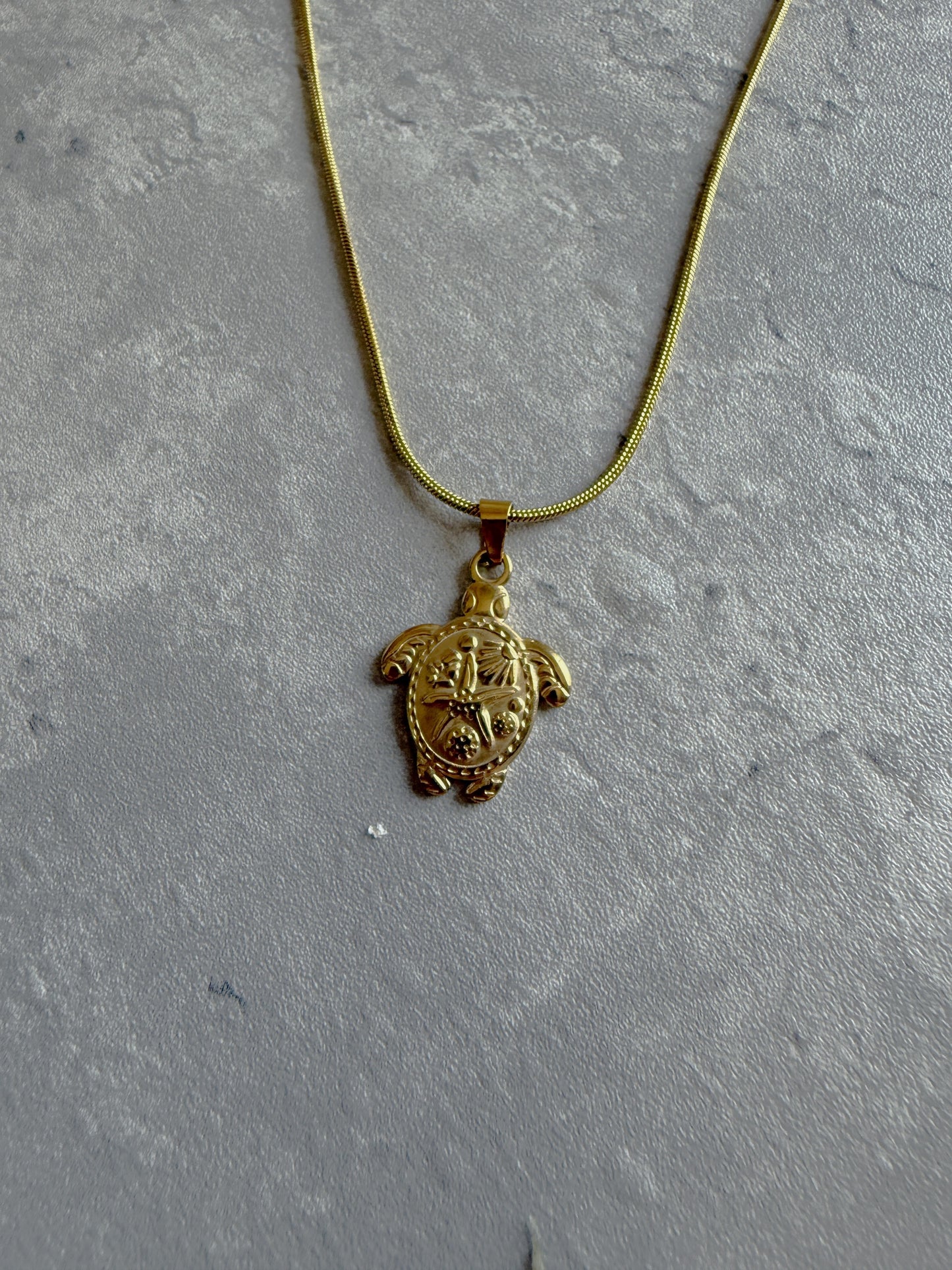 Gold turtle pendant necklace on a gray textured surface