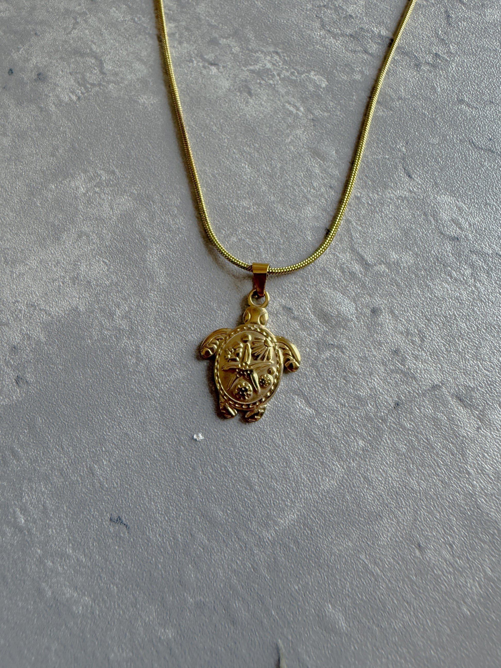 Gold turtle pendant necklace on a gray textured surface