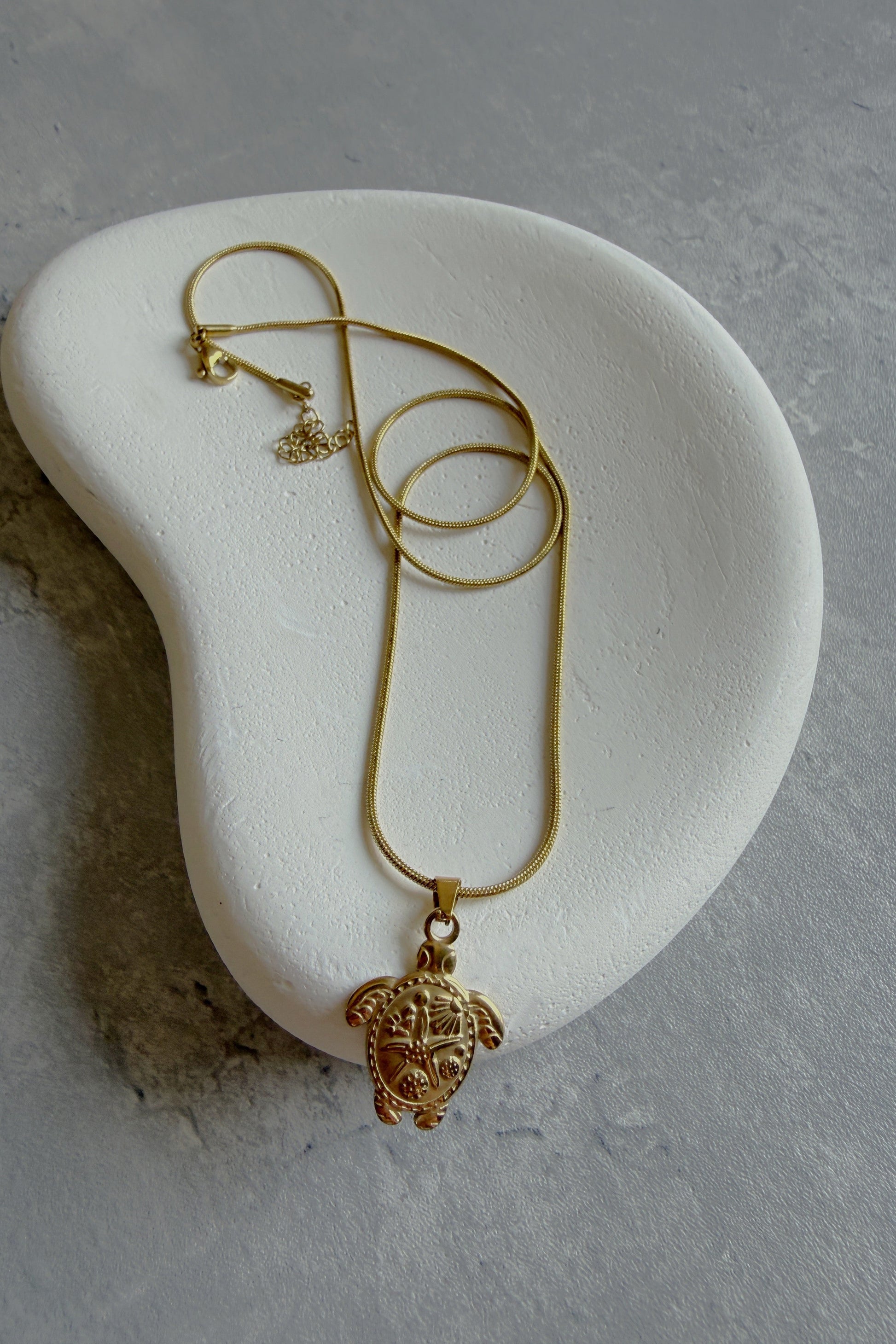 Gold necklace with a turtle pendant on a white stone surface