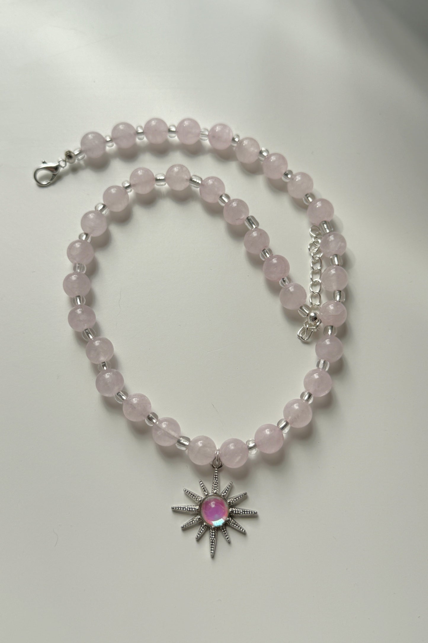 Necklace with pink beads and a sun-shaped pendant on a white background