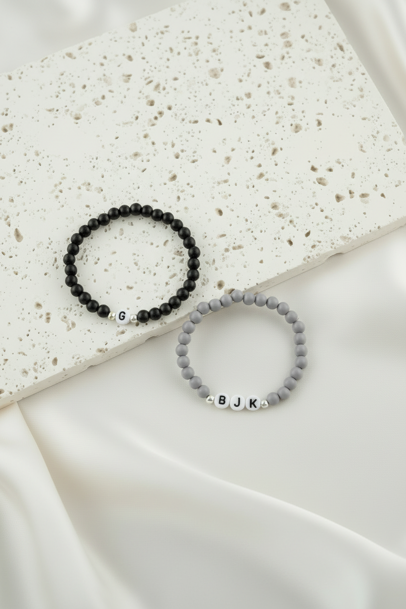 Two beaded bracelets with initials on a textured surface
