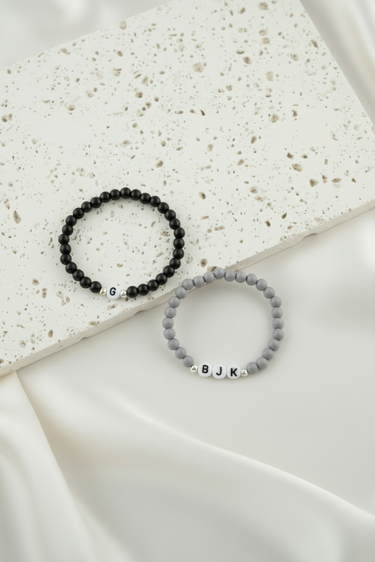 Two beaded bracelets with initials on a textured surface
