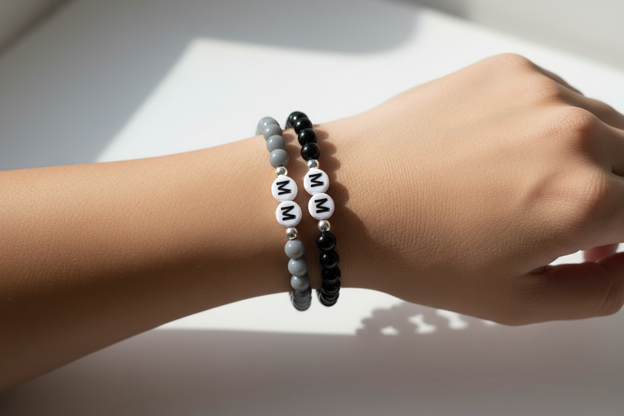 Hand wearing three bracelets with letter beads on a light background