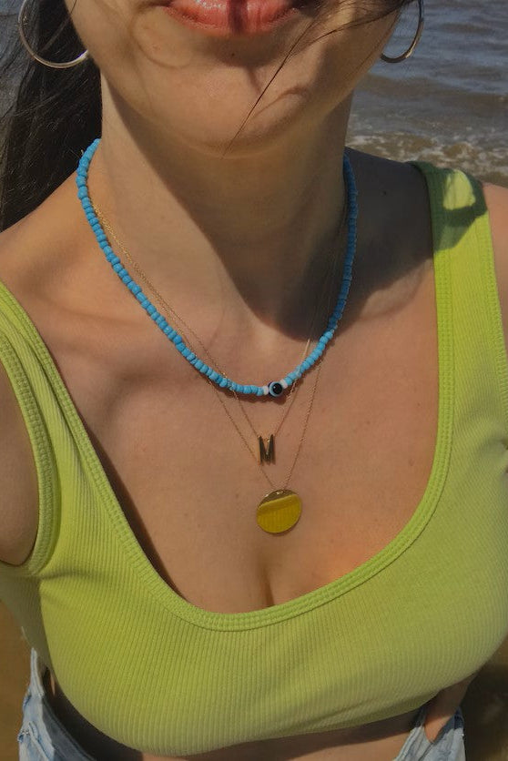 Woman wearing a green top and blue necklace by the beach