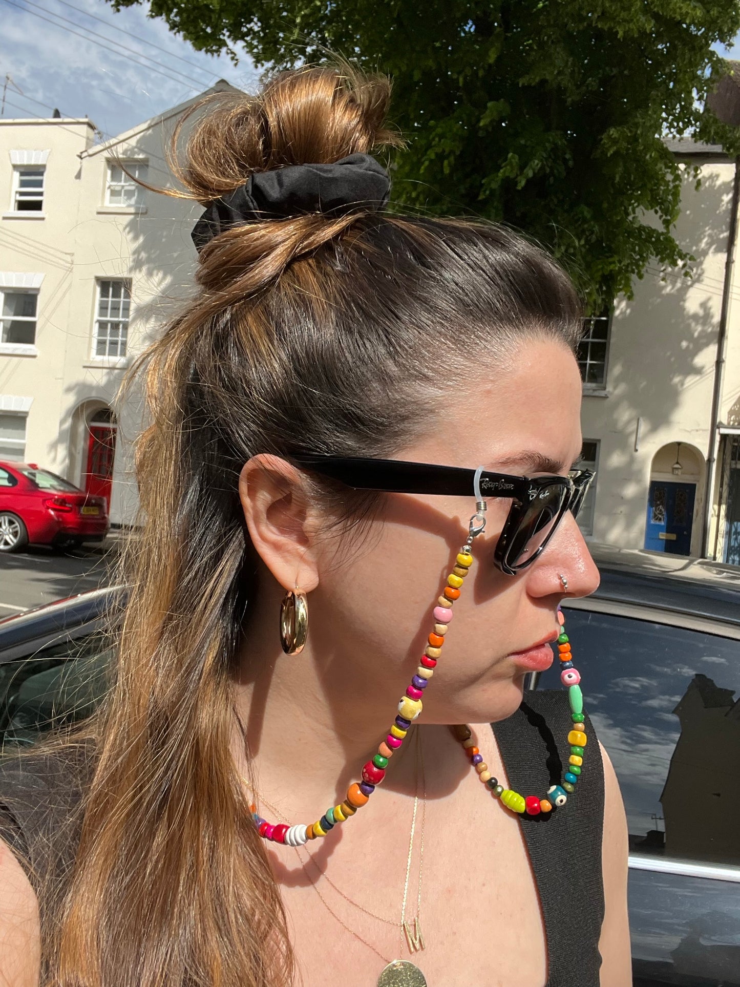 A girl on the street models the Wooden Beaded Sunglasses Chain with black sunglasses. The chain is stylishly draped around her neck, complementing her look against the urban backdrop.